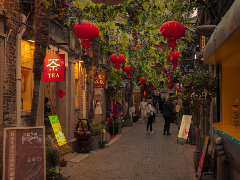 Lively old Shanghai alleyway decorated with red lanterns, tea shop signs, and visitors enjoying the vibrant atmosphere.