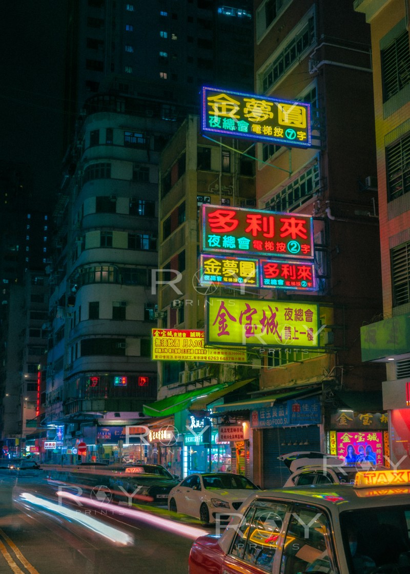 Busy Kowloon street with colorful neon signs, moving cars, and bustling nightlife.